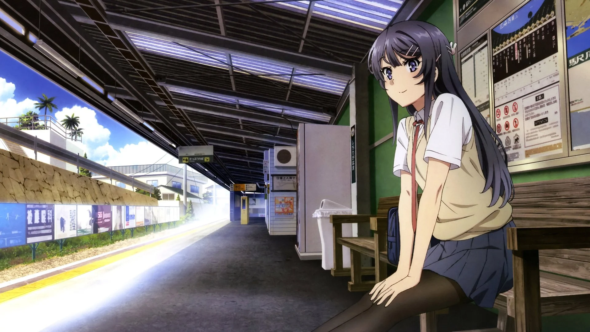 Mai Sakurajima assise sur un quai de gare au bord de la mer, en uniforme scolaire