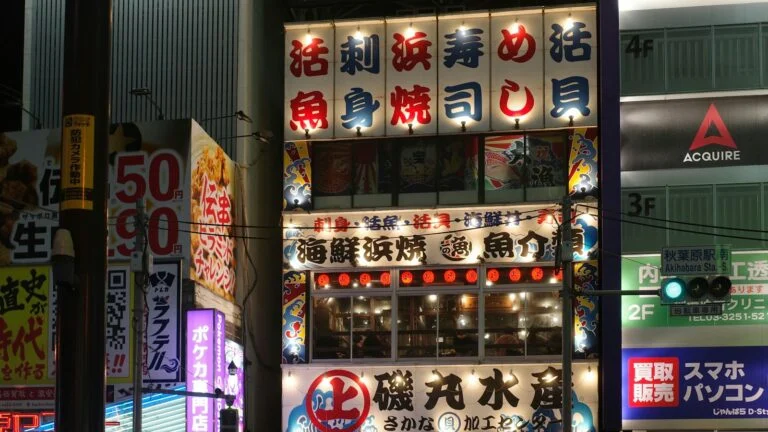 Façade d’un restaurant de Tokyo la nuit, couverte d’enseignes lumineuses en kanji et en katakana