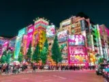 Passants dans une rue d’Akihabara à Tokyo la nuit, sous les enseignes lumineuses du quartier de l’anime