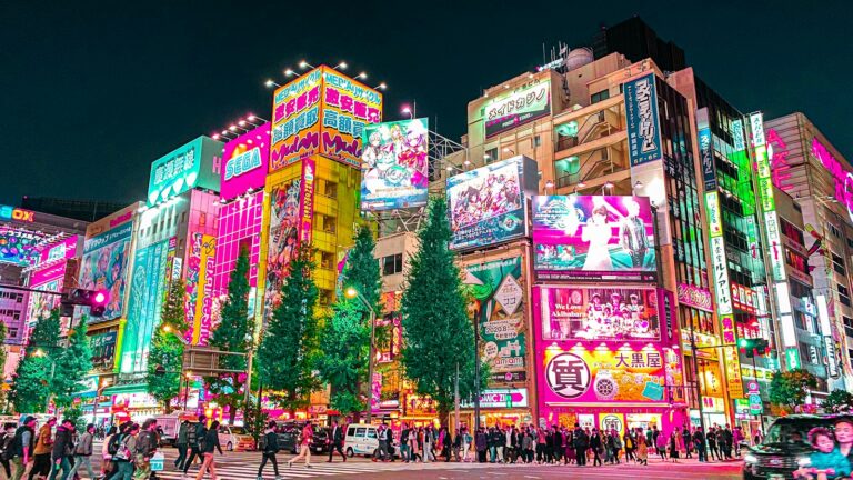 Passants dans une rue d’Akihabara à Tokyo la nuit, sous les enseignes lumineuses du quartier de l’anime
