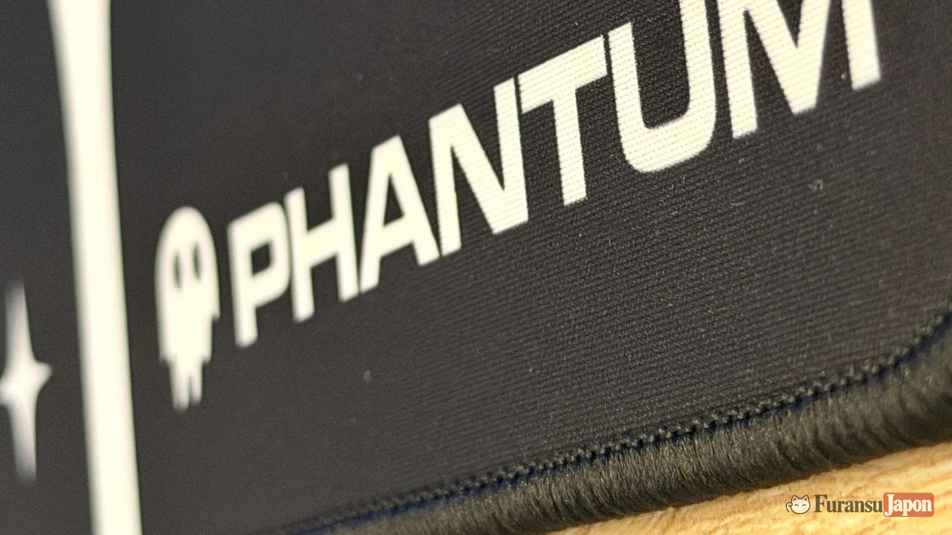 Gros plan sur le bord cousu et le logo Phantum du tapis Noctis, avec la trame de la surface en microfibre